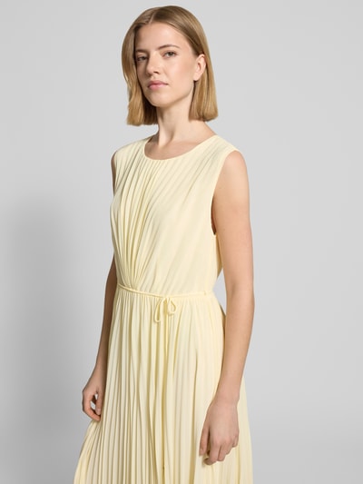 Frauenmodel trägt Regular Fit Kleid mit Plissee von s.Oliver BLACK LABEL in Optik: Unifarben, Midi-Länge, Rundhals-Ausschnitt, Nahtreißverschluss, Bindeband, ohne Ärmel, Materialverarbeitung: Plissee, zartes Gelb, fließende Plisseestruktur, Ganzkörperansicht von vorne.