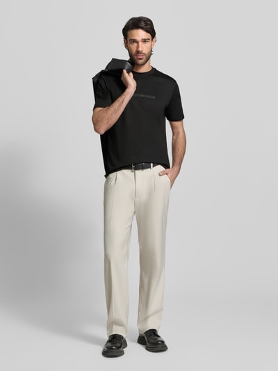 Männermodel trägt Regular Fit T-Shirt mit Logo-Detail von Emporio Armani in Schwarz, dazu helle Stoffhose, Rundhalsausschnitt, Ganzkörperansicht von vorne.