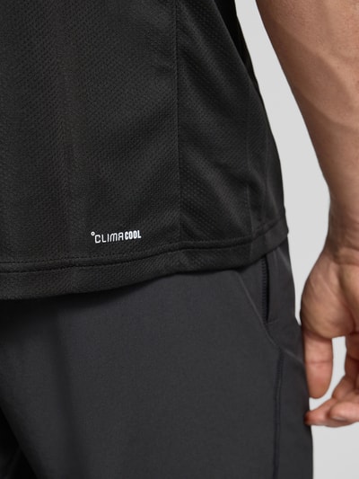Männermodel trägt schwarzes T-Shirt mit Label-Print von adidas Training, Regular Fit, Nahaufnahme Oberkörper, Textur leicht strukturiert.