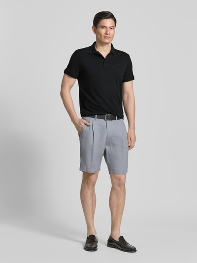 Männermodel trägt Regular Fit Poloshirt mit Knopfleiste Modell 'Carlosjuan' von JOOP! Collection aus Baumwoll-Mix mit Stretch-Anteil, Polokragen, Rückenlänge bei Größe M 69 cm, schwarze Farbe, glatte Struktur, Ganzkörperansicht von vorne.