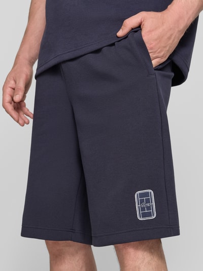 Männermodel trägt Relaxed Fit Sweatshorts aus katoenmix van Lacoste in donkerblauw met gestikte patch heren Sweatshorts, detailaufnahme rechterbeen.