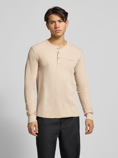 Męski model nosi Regular Fit Langarmshirt aus reiner Baumwolle od Tommy Jeans, jednokolorowy, fakturowany wzór, okrągły dekolt, logo, elastyczne rękawy, widok z przodu na całe ciało.