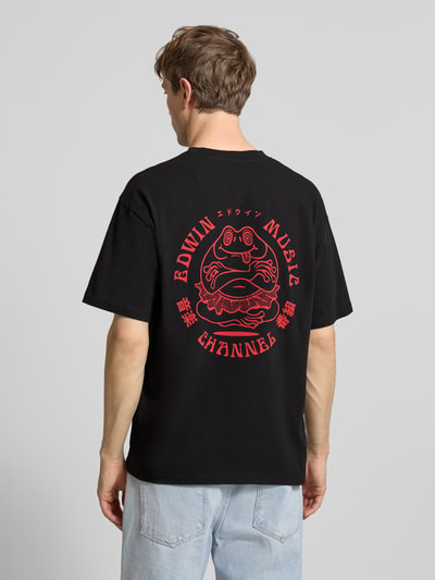 Männermodel trägt T-Shirt aus reiner Baumwolle Modell 'MUSIC CHANNEL' von Edwin in Schwarz mit rotem Print, Ganzkörperansicht Rückansicht.