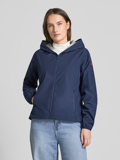 Frauenmodel trägt dunkelblaue Regular Fit Jacke mit Zweiwegereißverschluss Modell 'Stella' von SAVE THE DUCK, Eingrifftaschen, Ganzkörperansicht von vorne. Rückenlänge 60 cm, Schulterbreite 42 cm, Brustweite 52 cm, Ärmellänge 64 cm.
