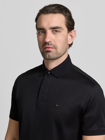 Männermodel trägt Poloshirt mit kurzer Knopfleiste von Emporio Armani, schwarz, Regular Fit, Label-Stitching, Nahaufnahme Oberkörper.
