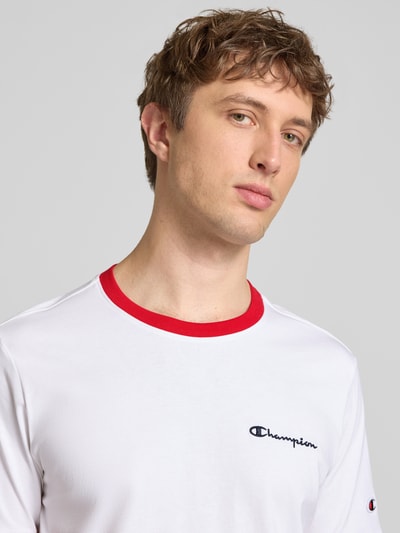 Männermodel trägt T-Shirt mit Rundhalsausschnitt und Label-Stitchings von CHAMPION, reine Baumwolle, weiß mit rotem Kragen, Nahaufnahme Oberkörper.