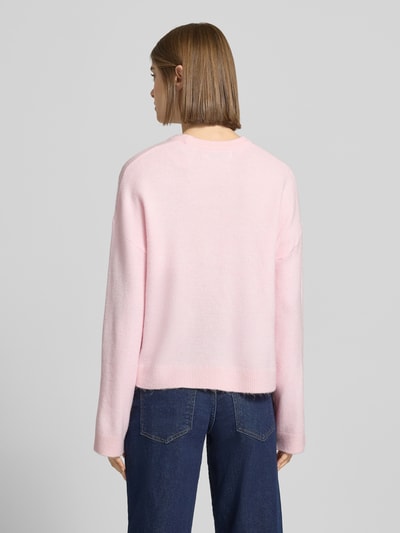 Frauenmodel trägt Relaxed Fit Strickpullover mit Crew Neck Modell 'SIMONI' von Only in Rosa, melierte Optik, Rippenabschlüsse, Ganzkörperansicht Rückansicht.