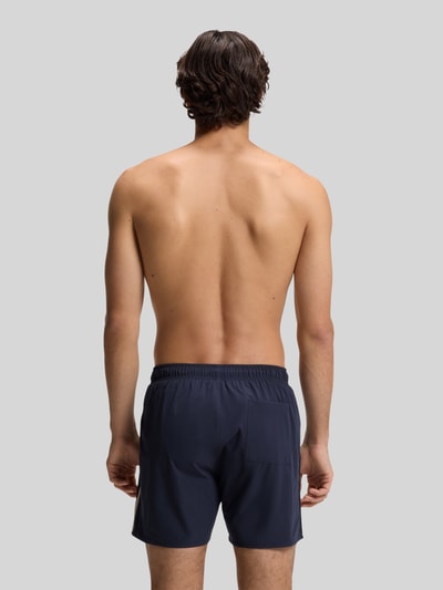 Mannenmodel draagt Badeshorts met tunnelkoord model 'ICONIC' van BOSS in effen look met labelprint, contraststrepen, elastische tailleband, zijzakken en achterzak; volledige rugaanzicht.