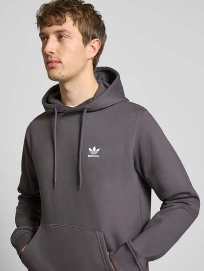 Männermodel trägt Regular Fit Hoodie aus Baumwoll-Mix von adidas Originals in Uni-Grau mit Logo-Stitching, Nahaufnahme Oberkörper.