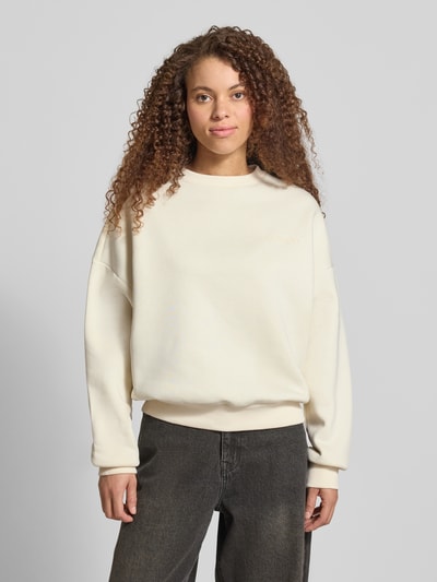 Modelka kobieca nosi Basic Sweater mit Rundhalsausschnitt und Bündchen am Ärmel od Review, kremowy, oversize, logotyp, widok z przodu, ujęcie całej sylwetki.