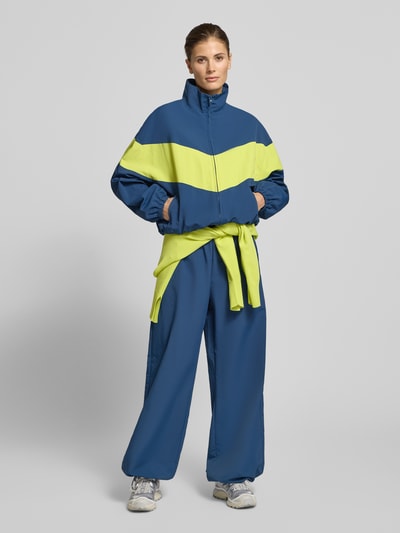 Frauenmodel trägt Nylon-Ballonhose im 90s-Stil - curated by Tinvcb von Tinvcb in Blau mit entspannter Passform, elastischem Bund und Eingrifftaschen, Bundweite XS/S 34 cm, Innenbeinlänge 78 cm, Ganzkörperansicht von vorne.