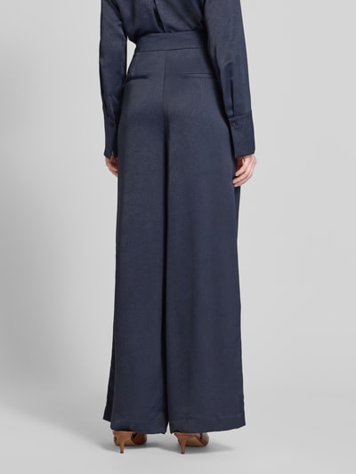 Kobieta modelka nosi Wide Fit Stoffhose mit Strukturmuster od Christian Berg Cocktail, ciemnoniebieski kolor, strukturalny wzór, motyw kwiatowy, zakładki w pasie, zapięcie na haftkę i zamek, szerokość w rozmiarze 36: 40 cm, długość nogawki od wewnątrz: 80 cm, widok całej sylwetki z tyłu.