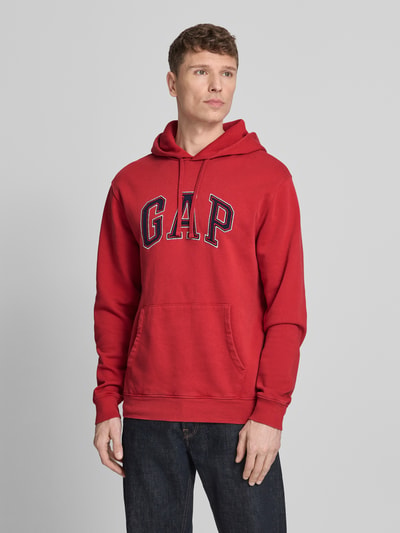 Mannenmodel draagt Hoodie mit Logo und Känguru-Tasche van GAP in rood, regular fit, katoenmix, logo en buidelzak, vooraanzicht heuphoogte.