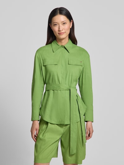 Frauenmodel trägt Bluse aus Leinen-Mix mit Brusttaschen von Marc Cain in Grün, taillierte Passform, Stoffband, Umlegekragen, Nahaufnahme Oberkörper. Rückenlänge bei Größe 36: 69 cm, Ärmellänge bei Größe 36: 55 cm, Leinen-Viskose-Anteil.