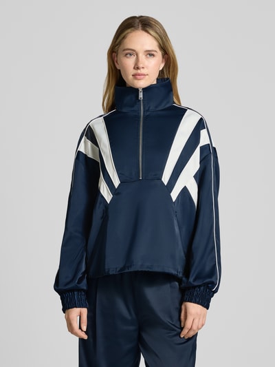 Modelka kobieca nosi Regular Fit Anorak mit Viskose-Anteil Modell 'Bicca' od Gestuz, granatowy z białymi pasami, krój regular fit, elastyczna mieszanka materiałów, stójka z zamkiem, kieszenie na zamek, elastyczne mankiety, długość tyłu 60 cm, szerokość ramion 55 cm, szerokość w rozmiarze 36: 69 cm, długość rękawa 65 cm, całkowity widok z przodu.