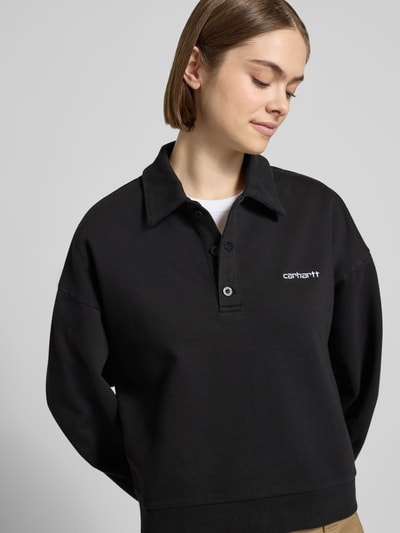 Frauenmodel trägt schwarzes Damen Sweatshirt mit Polokragen, Knopfleiste und Label-Stitching Modell 'Brenta' von Carhartt Work In Progress aus Reine Baumwolle im Relaxed-Fit, Nahaufnahme Oberkörper.