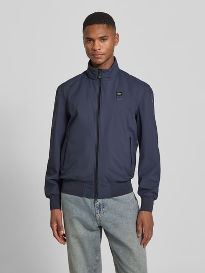 Männermodel trägt Jacke mit Label-Patches Modell 'Anson' von Blauer Usa in Dunkelblau, gerader Schnitt, Stehkragen, vorne Ganzkörperansicht.