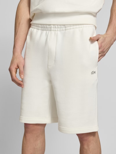 Männermodel trägt Relaxed Fit Sweatshorts aus reiner Baumwolle von Lacoste in Weiß mit Logo-Detail, elastischem Bund, Nahaufnahme Oberkörper.