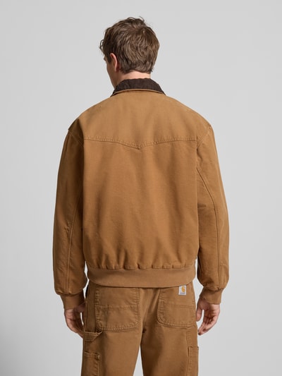 Męski model nosi Jacke mit Reißverschluss und Label-Detail von Carhartt Work In Progress z bawełny ekologicznej, krój regular fit, wykładany kołnierz, zamek błyskawiczny, wpuszczane kieszenie, detal z logo, długość tyłu w rozmiarze M: 70 cm, szerokość ramion w rozmiarze M: 56 cm, szerokość klatki piersiowej w rozmiarze M: 65 cm, długość rękawów w rozmiarze M: 67 cm, brązowe odcienie, tekstura gładka, widok całej sylwetki od tyłu
