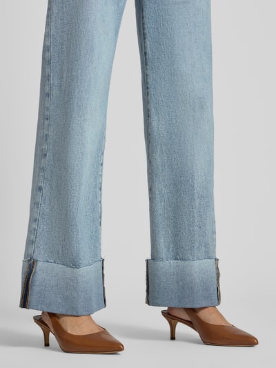 Frauenmodel trägt Wide Fit Jeans aus reiner Baumwolle Modell 'Rey' von GUESS in hellem Blau, texturierte Baumwolle, Nahaufnahme Beine, 5-Pocket-Design, breite umgeschlagene Säume, Damen Jeans von GUESS, KI-modifiziertes Bild.