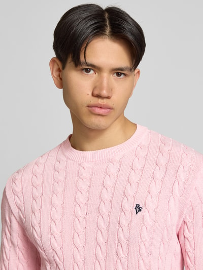 Männermodel trägt Strickpullover mit Zopfmuster und Logo-Stitching von REVIEW aus Baumwoll-Mix in Rosa, Nahaufnahme Oberkörper.