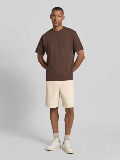 Męski model nosi Regular Fit Sweatshorts aus Baumwoll-Mix Modell 'JACE' von SELECTED HOMME, jednolity kremowy kolor, sztruks, boczne kieszenie, tylna kieszeń, szlufki, tunel z troczkiem, krój regular fit, widok całej sylwetki z przodu.