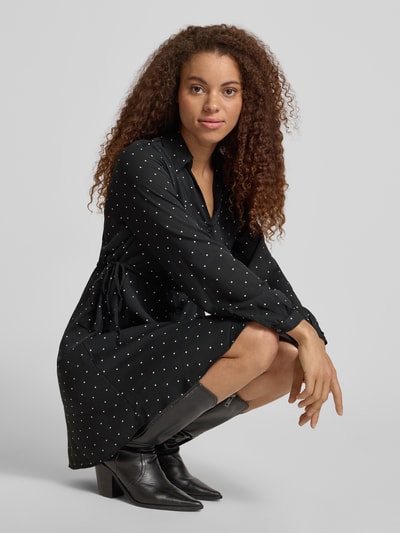 Kobiece model nosi Tailliertes Freizeitkleid mit Allover-Muster Modell 'ALYNN' od Only, efekt: wzór na całej powierzchni, krój: taliowany, długość: mini, dekolt: wysokie zapięcie, ściągacz w talii, listwa guzikowa, długi rękaw z mankietem, kolor czarny z białymi akcentami, materiał gładki, widok całofigurowy z przodu.