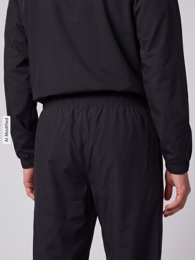Männermodel trägt schwarze Regular Fit Trainingshose mit Logo-Patch von Lacoste, Textur glatt, Ganzkörperansicht Rückansicht, Herren Trainingshose von Lacoste Sport, KI-modifiziertes Bild.