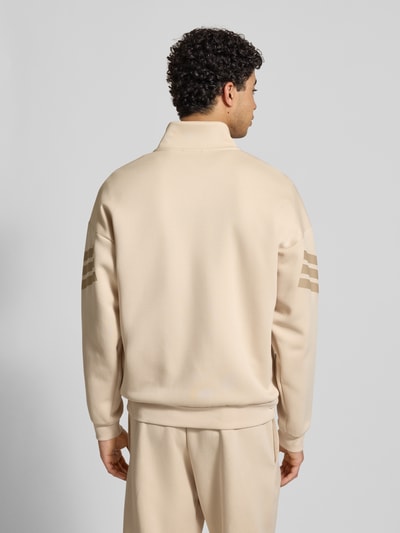 Mannenmodel draagt Regular Fit Sweatjacke mit Stehkragen van adidas Sportswear in beige katoenmix met logoprint en elastische boorden, ruglengte bij maat M 69 cm, mouwlengte 54 cm. Ganzkörperansicht Rückansicht.