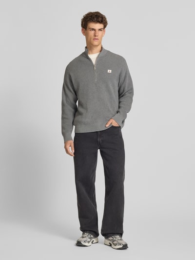Männermodel trägt Loose Fit Troyer mit gerippten Abschlüssen von Calvin Klein Jeans in Grau mit kurzem Reißverschluss, Ganzkörperansicht von vorne.