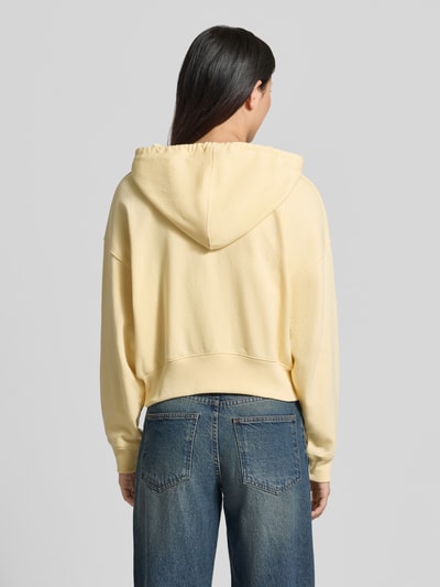 Vrouwenmodel draagt Regular Fit Sweatjacke mit Logo-Stitching Modell 'Heritage' van GAP in lichtgeel katoenmix met capuchon, kangoeroezak en elastische boorden. Ganzkörperansicht Rückansicht.