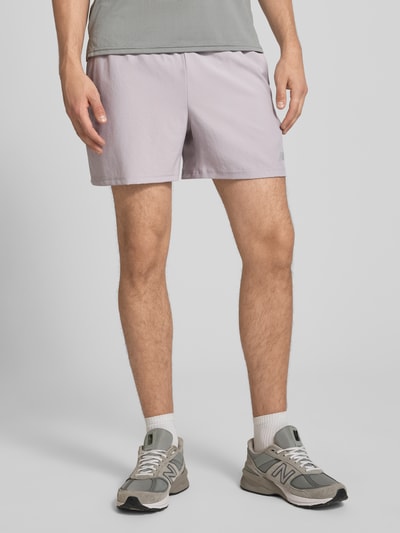Männermodel trägt Shorts mit elastischem Bund und Logo von New Balance in Hellgrau, Regular Fit, Nahaufnahme Oberschenkel, Vorderansicht.