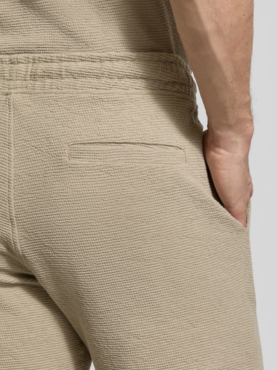 Mężczyzna nosi Regular Fit Poloshirt aus Baumwoll-Mix von MCNEAL, mieszanka bawełny i elastanu, pika waflowa, kolor beżowy, detal tylnej kieszeni, zbliżenie na biodro, nahaufnahme biodra.