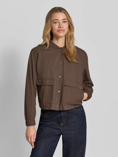 Frauenmodel trägt Jacke mit Pattentaschen von camel active, mieszanka bawełny, krój regular fit, stójka, listwa guzikowa, kieszenie z patką, długość tyłu w rozmiarze 36: 54 cm, szerokość ramion w rozmiarze 36: 43 cm, szerokość klatki piersiowej w rozmiarze 36: 55 cm, długość rękawów w rozmiarze 36: 58 cm; brązowy, gładka tkanina, kieszenie i guziki, Ganzkörperansicht von vorne.