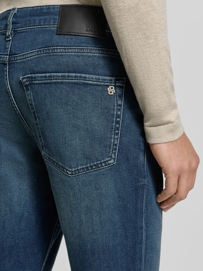 Männermodel trägt Slim Fit Jeans aus Baumwoll-Mix Modell 'SMU ONYX' von BOSS Orange, blauer Denim, Label Patch, Nahaufnahme Rückansicht.