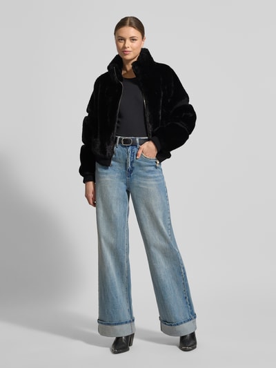 Frauenmodel trägt Jacke mit Teddyfell und gerippten Abschlüssen von Guess, schwarz, gerader Schnitt, Stehkragen, Reißverschluss, Ganzkörperansicht von vorne. Rückenlänge 56 cm, Schulterbreite 38 cm, Brustweite 53 cm, Ärmellänge 61 cm.