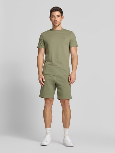 Männermodel trägt Regular Fit T-Shirt aus reiner Baumwolle von Lacoste in Unifarben mit Rundhals und kurzem Arm, Ganzkörperansicht von vorne.