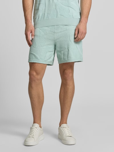 Männermodel trägt Regular Fit Sweatshorts aus Baumwoll-Mix Modell 'ASURFER' von BOSS Orange in Optik: Unifarben mit Struktur-Muster, Label-Patch, Bundabschluss elastisch mit Tunnelzug und Eingrifftaschen, Materialverarbeitung: Frottee, Farbe helles Mint, Ganzkörperansicht von vorne.