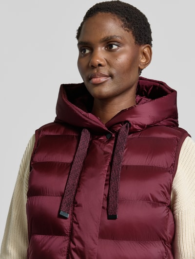 Frauenmodel trägt Regular Fit Weste in Stepp-Optik von FUCHS SCHMITT in Dunkelrot mit Kapuze und Reißverschlusstaschen, Nahaufnahme Oberkörper. Rückenlänge 77 cm, Schulterbreite 41 cm, Brustweite 51 cm.