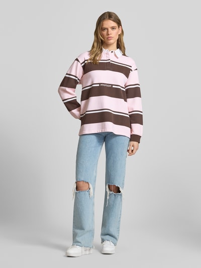 Frauenmodel trägt Sweatshirt mit Polokragen Modell 'MORELLA' von Pegador, rosa-braun gestreift, Reine Baumwolle, Loose-Fit, Logo-Print, Ganzkörperansicht von vorne.