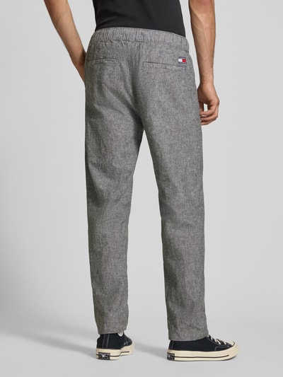 Männermodel trägt Regular Fit Weite Hose aus Leinen-Baumwoll-Mix von Tommy Jeans in melange optik mit label stitching, elastischer taille, flammgaren textuur, zijzakken en achterzakken, productfoto, ganzkörperansicht rückansicht.