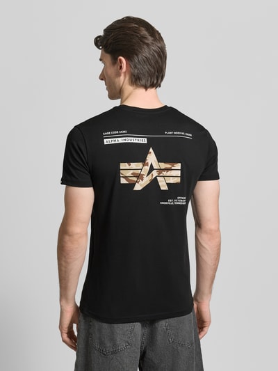 Männermodel trägt schwarzes T-Shirt mit Label-Patch Modell 'Camo' von Alpha Industries aus gewachster Baumwolle, Rückansicht, Ganzkörperansicht.