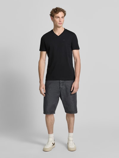 Mannelijk model draagt zwart Regular Fit T-shirt uit zuivere katoen van s.Oliver RED LABEL, gecombineerd met donkere shorts, geheellichaamsaanzicht van voren.