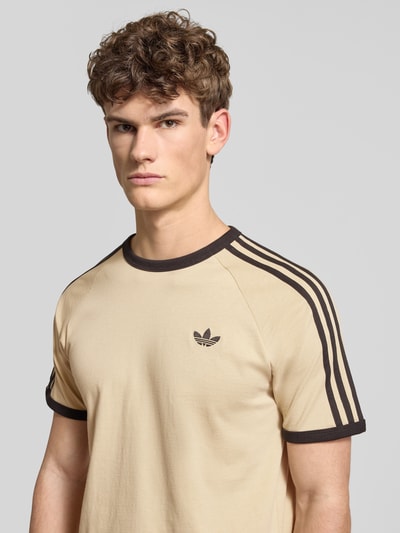 Męski model nosi T-shirt im Retro-Look mit Rundhalsausschnitt od adidas Originals z logo, bawełna, krój regular fit, długość tyłu 70 cm, nahaufnahme oberkörper.