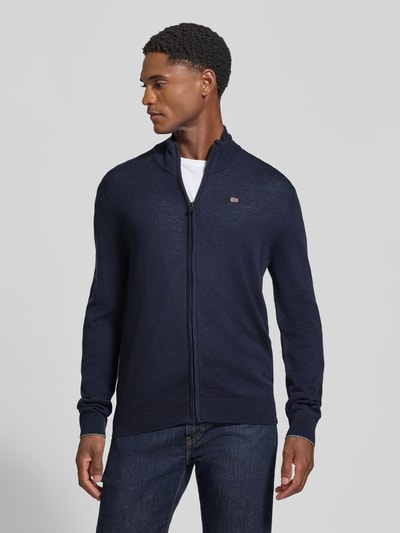 Männermodel trägt Strickjacke mit Logo-Stitching Modell 'DAMAVAND' von Napapijri, dunkelblau, Reißverschluss, reine Wolle, Ganzkörperansicht von vorne.