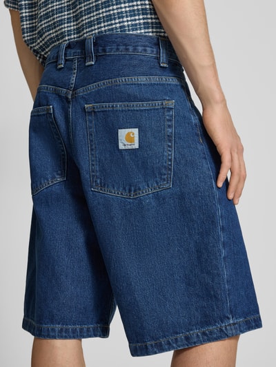 Männermodel trägt Jeansshorts mit Eingrifftaschen Modell 'Brandon' von Carhartt Work In Progress aus Reine Baumwolle, Relaxed-Fit, Ganzkörperansicht Rückansicht.