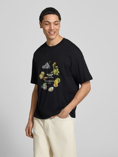 Männermodel trägt T-Shirt mit Rundhalsausschnitt von Jack & Jones, Reine Baumwolle, Regular-Fit, Print, schwarze Grundfarbe, Ganzkörperansicht von vorne. Rückenlänge bei Größe M: 70 cm.