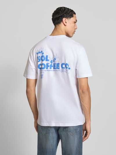 Męski model nosi Relaxed Fit T-Shirt aus reiner Bio-Baumwolle Modell 'FRED' von Only & Sons, białe, niebieski nadruk na plecach, koszulka gładka, bawełna organiczna, zdjęcie całej sylwetki z tyłu.