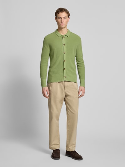 Męski model nosi Regular Fit Strickjacke mit Kaschmir-Anteil von FTC Cashmere, mieszanka bawełny i kaszmiru, wykładany kołnierz, listwa guzikowa, elastyczne wykończenia, długość tyłu 71 cm, długość rękawów 68 cm, beżowe spodnie, brązowe buty, krój regular fit, widok całej sylwetki z przodu