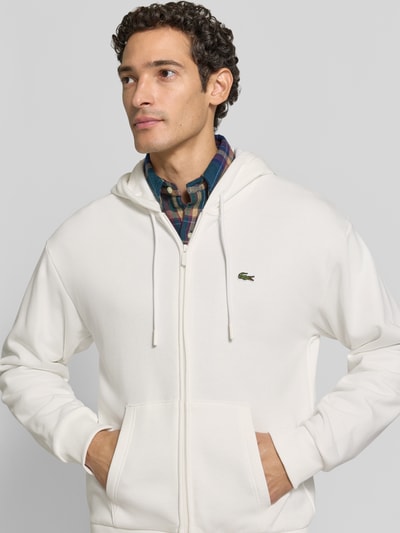 Männermodel trägt Regular Fit Sweatjacke aus Baumwoll-Mix von Lacoste in Weiß, glatte Textur, Nahaufnahme Oberkörper, Herren Sweatjacke von Lacoste.